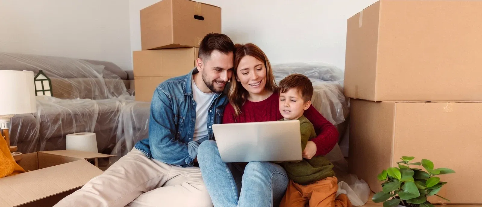Father, Mother and child using a laptop while sitting amongst moving boxes.